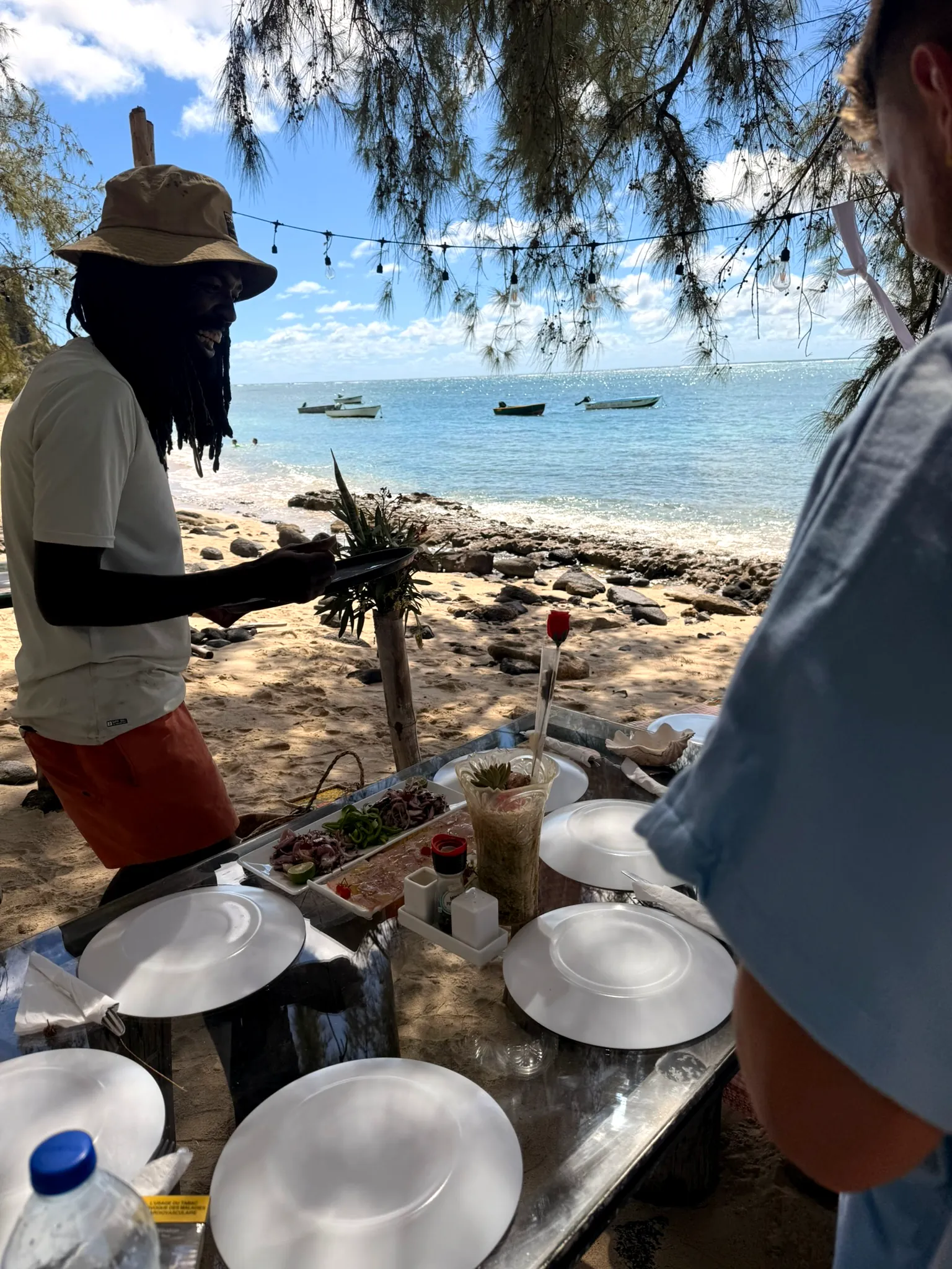 Le service du repas partagé chez Otentika, assiettes et plats posés face à la plage